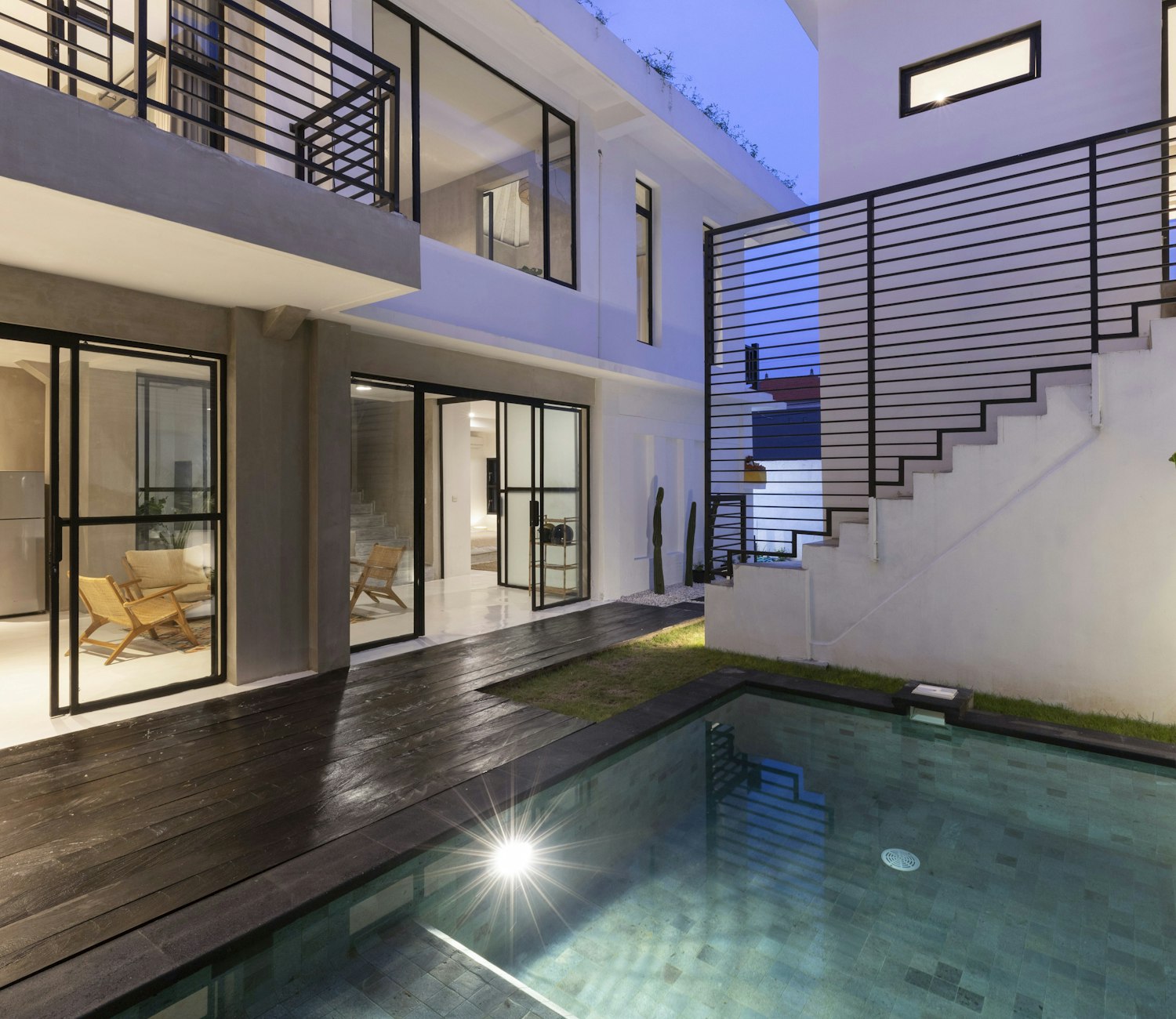 Contemporary home at dusk with floor-to-ceiling glazing and a timber deck around a softly lit pool